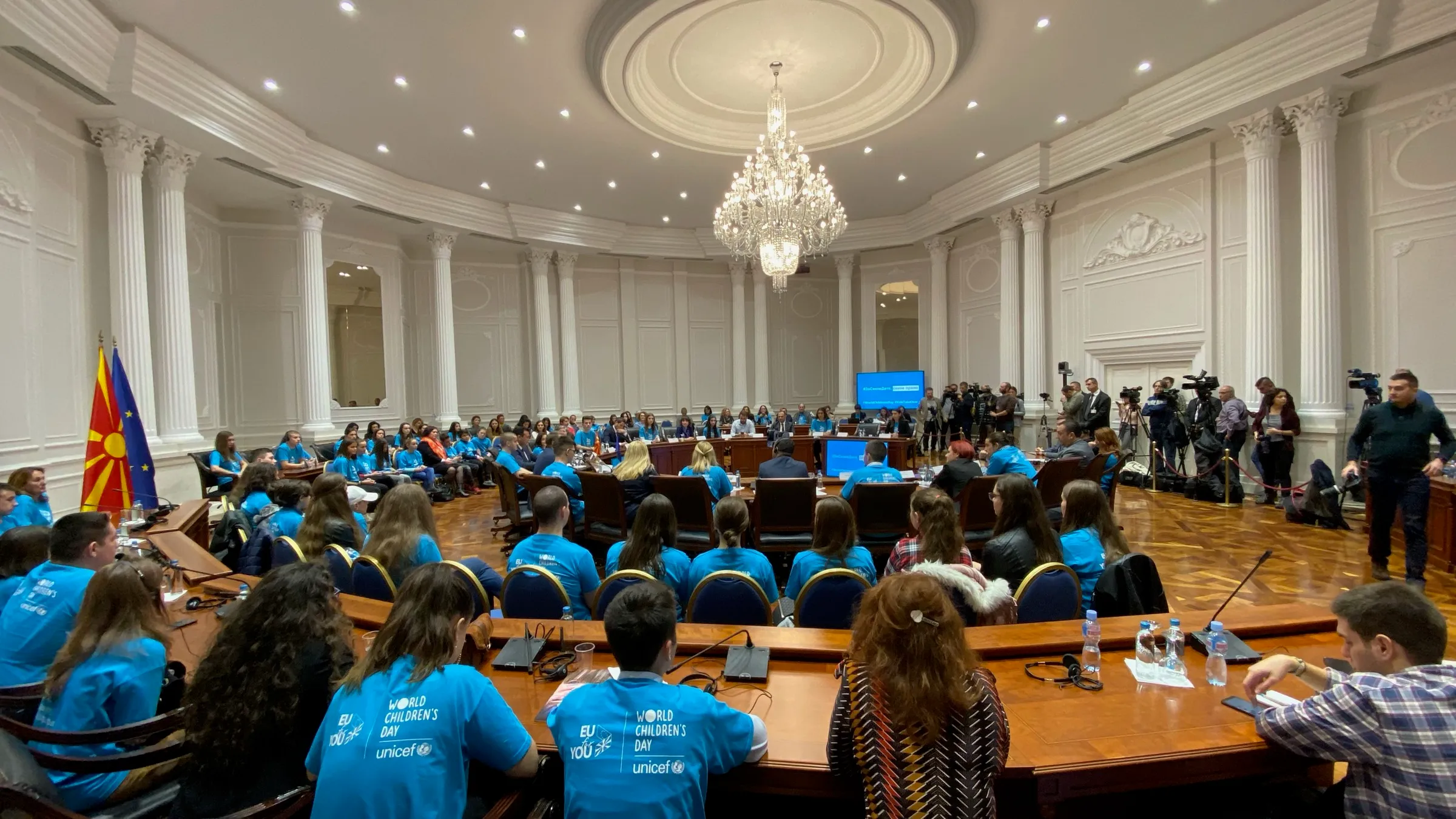 Children's Parliament session in the Parliament of North Macedonia, with the national flag and the EU flag in the foreground and participants in UNICEF World Children's Day shirts.